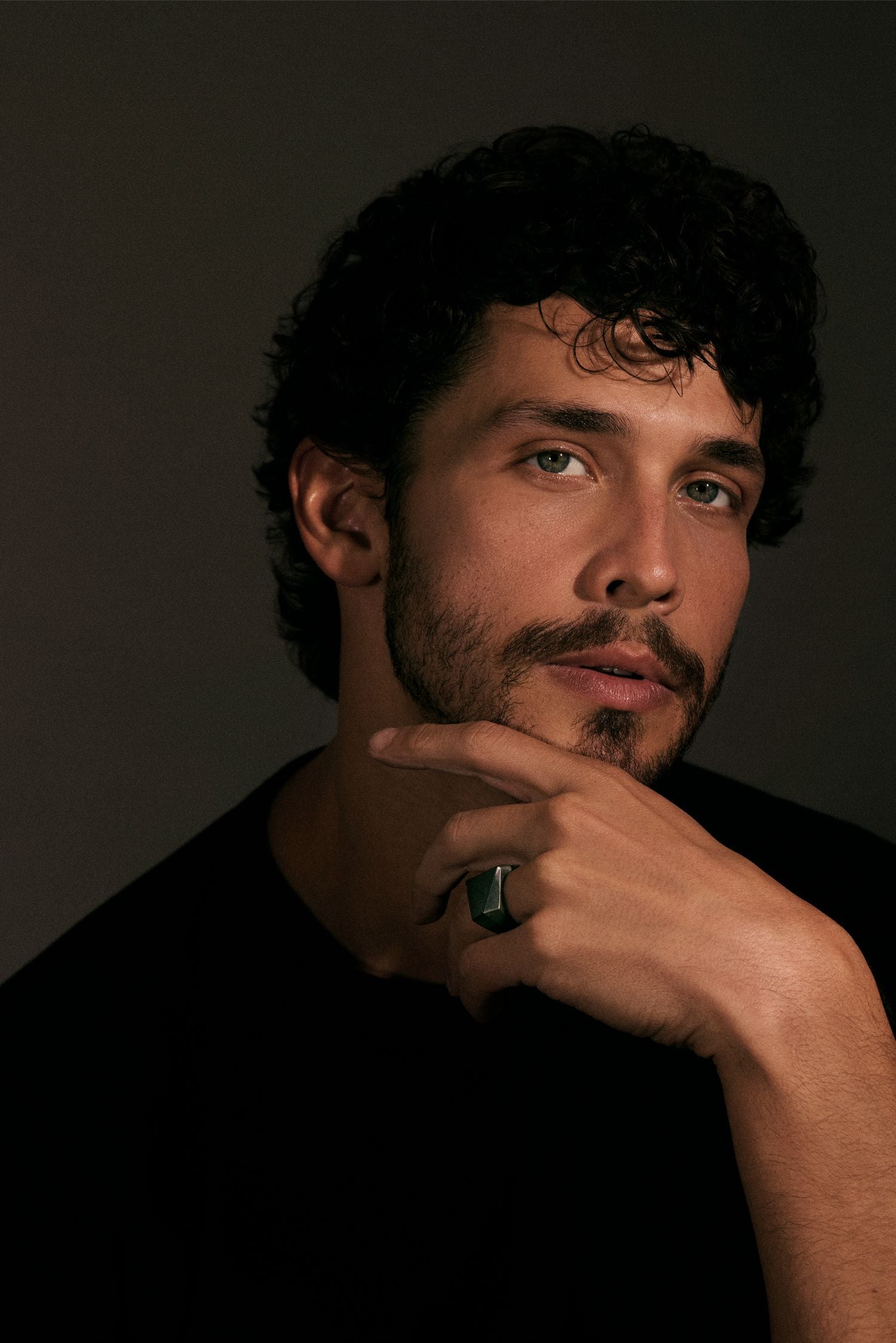 Man with a beard and mustache, wearing a black shirt, against a dark background.