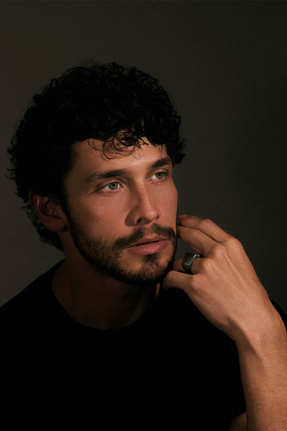 Man with dark hair and beard, wearing a black shirt, against a dark background.