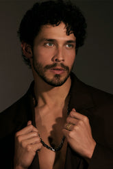 Man with a beard and curly hair wearing a dark shirt against a brown background