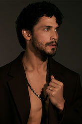 Man with a beard wearing a black suit jacket over an open shirt against a dark background