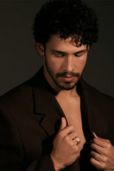 Man adjusting his brown jacket against a dark background