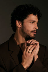Man with a beard and dark hair wearing a brown jacket against a dark background