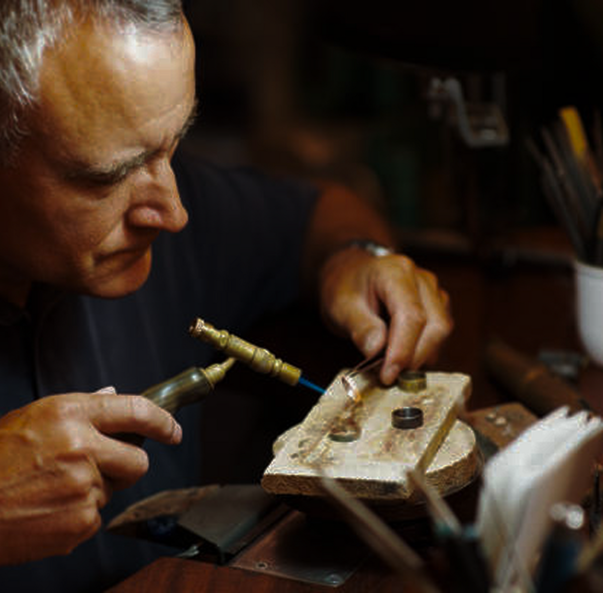 Artisan working on a gold ring with jewelry tools in a workshop setting on a workbench